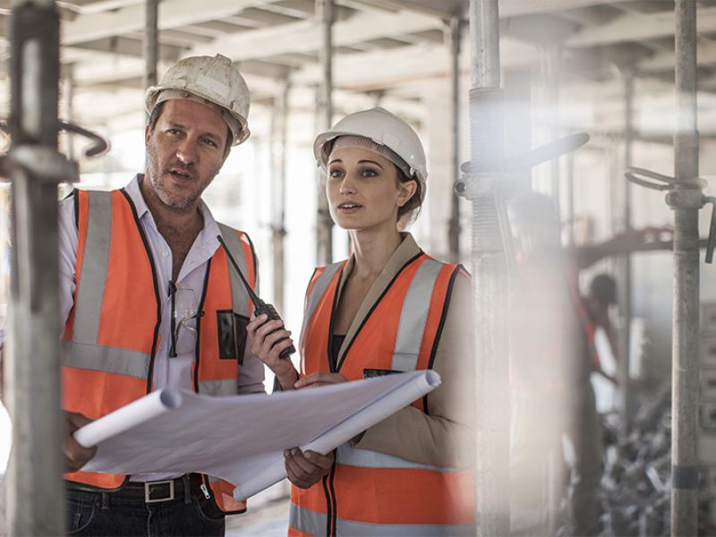 Female and male builders with blueprint on construction site